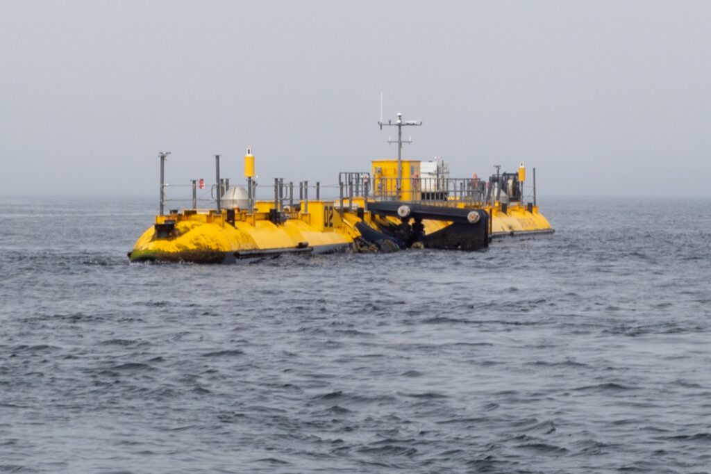 A large, segmented yellow and black Pelamis wave energy converter floating on dark gray water under an overcast sky.