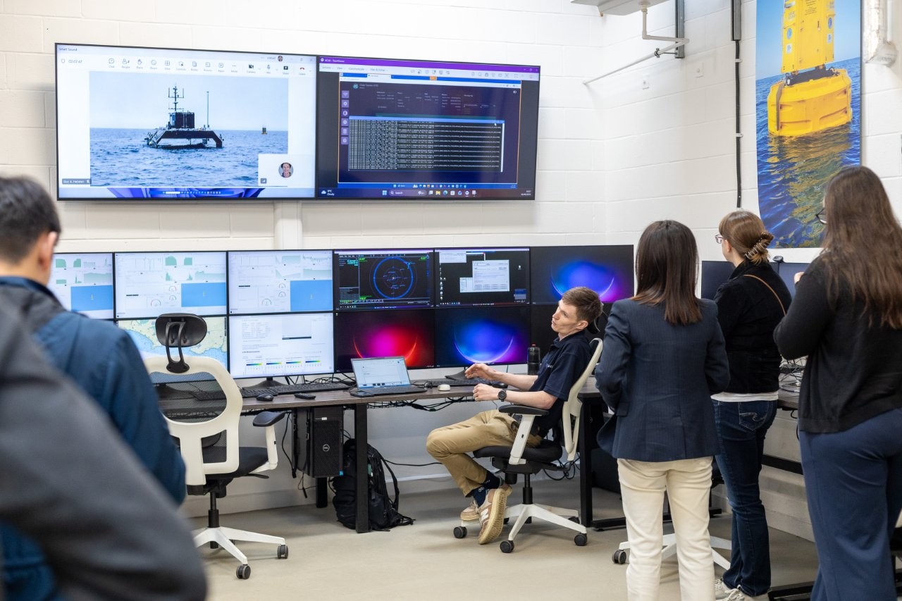 People in a control room looking at multiple computer screens displaying data, maps, and an unmanned surface vessel.