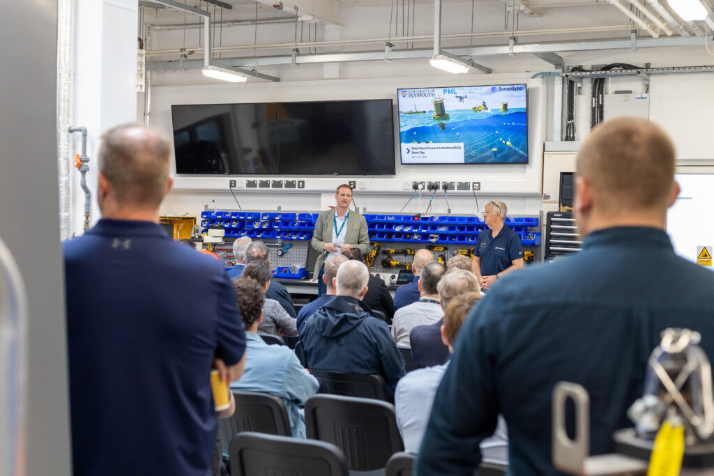 A man presents to an audience in a workshop, with a screen displaying 'Smart Sound Connect Subsurface Demo Day' and logos for University of Plymouth, PML, and Sonardyne.