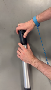 Hands assembling a black and silver cylindrical device, with a blue anti-static wrist strap on the right wrist.