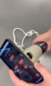 A person's hands holding a smartphone displaying an NFC control app and a cylindrical Seascape RT6-1000 device.