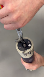 Close-up of hands using an RS PRO tool to tighten a screw on a beige and black cylindrical device with a label '3'.