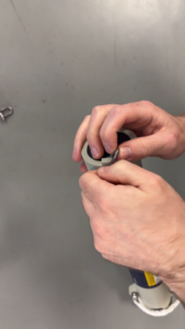 Close-up of hands inserting a small metal piece into the end of a light grey cylindrical object.