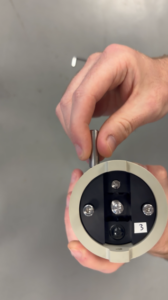Hands inserting a metal pin into a cylindrical device with a black faceplate and number 3.