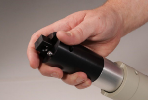 Close-up of a hand gripping a black and silver cylindrical precision tool with a square end and a small silver ball.