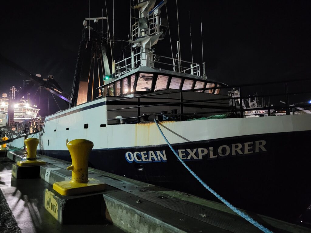 A large vessel named "OCEAN EXPLORER" docked at a pier at night, with yellow bollards in the foreground.