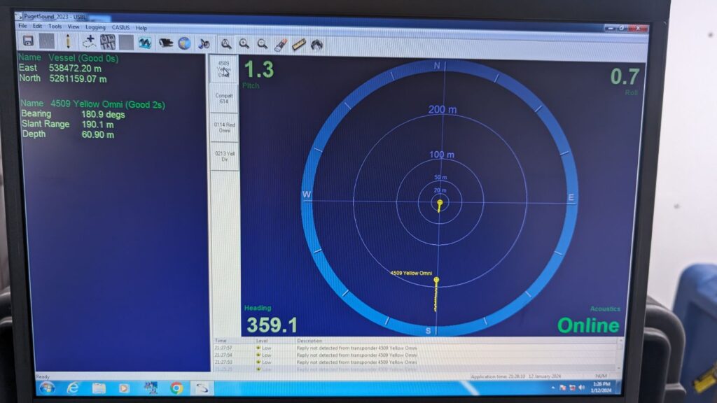 A computer screen displays a USBL acoustic positioning software interface with a circular sonar-like map, vessel data, and transponder information.